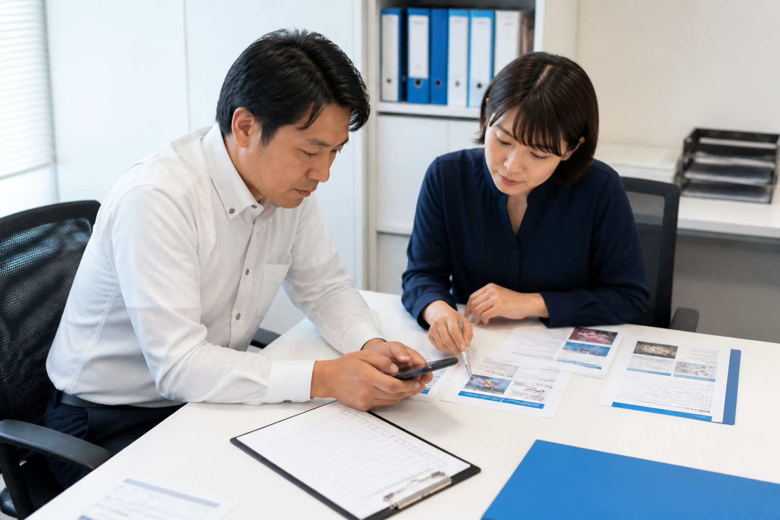 資料とスマートフォンを使ってSNS投稿を公開前確認する地方議員と広報担当者